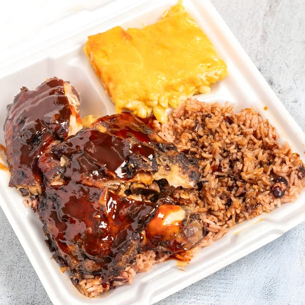 Top Taste Grill's jerk chicken with rice and peas, and mac and cheese in a takeout container.