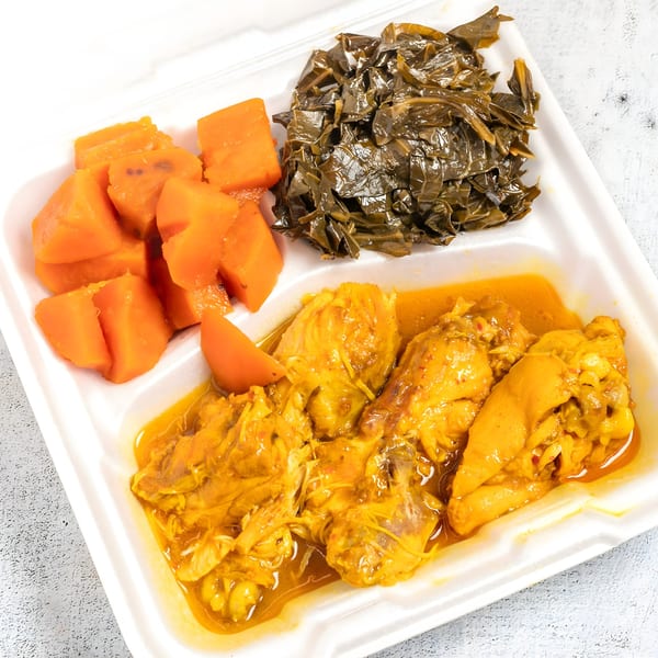 Curry chicken with collard greens and sweet potatoes in a white takeout container.