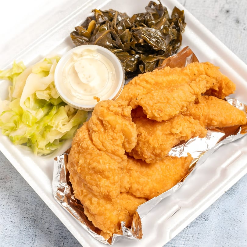 Fried chicken tenders with collard greens, cabbage, and dipping sauce in a styrofoam container.
