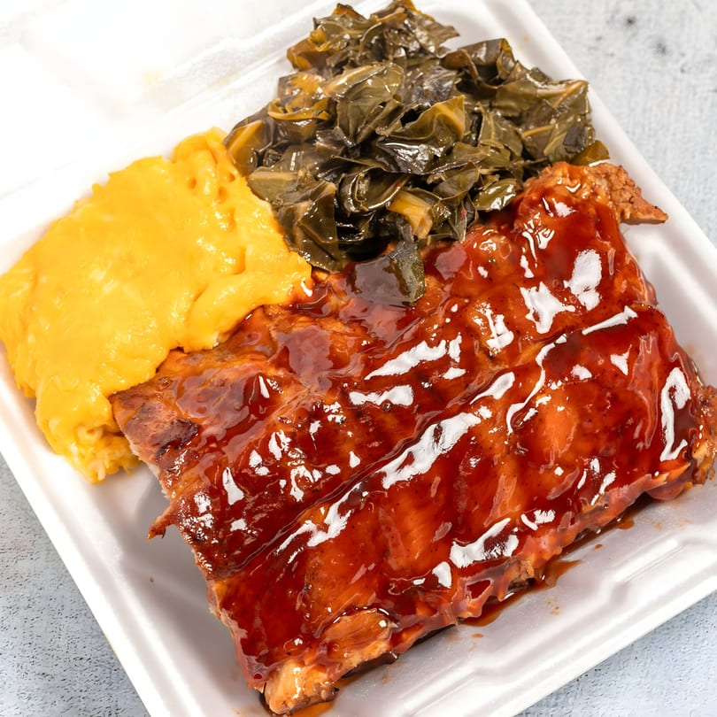 Top Taste Grill's Jamaican jerk ribs with mac and cheese and collard greens in a takeout container.