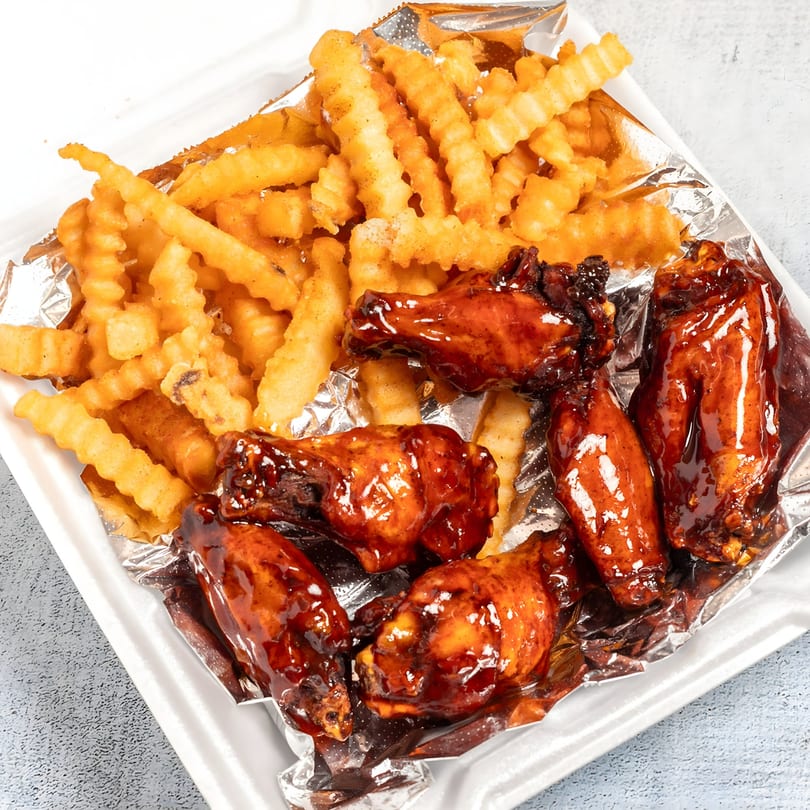 Top Taste Grill's Jamaican jerk chicken wings with barbecue sauce and crinkle-cut fries in a takeout container.