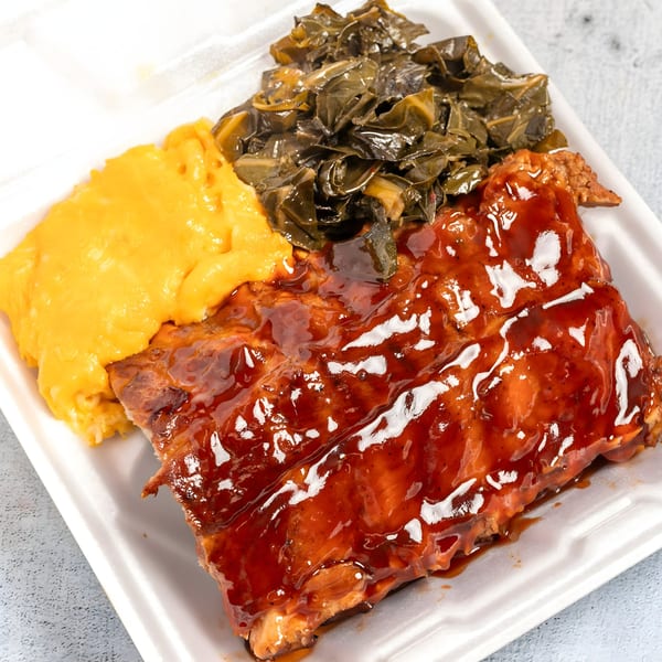 Top Taste Grill's jerk ribs with mac and cheese and collard greens in a takeout container.
